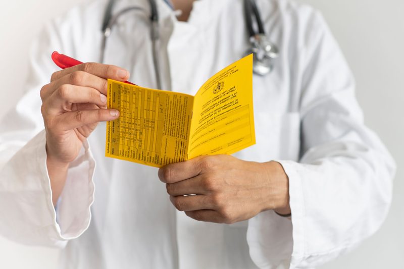Arzt oder Ärztin hält einen Internationalen Impfpasses samt Kugelschreiber in den Händen.